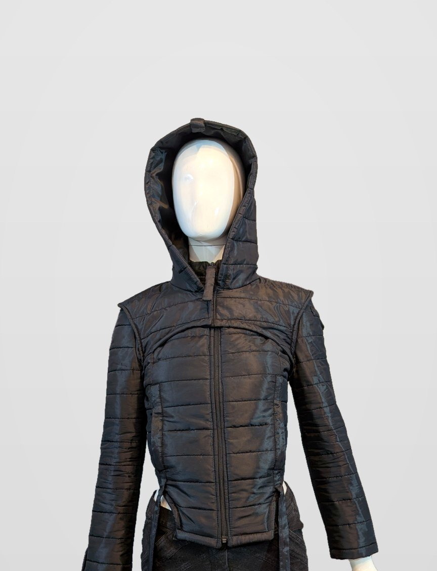 Black Nova Puffer — black futuristic quilted puffer jacket with hood on a mannequin, framed just below the jacket hem, pearl-grey background