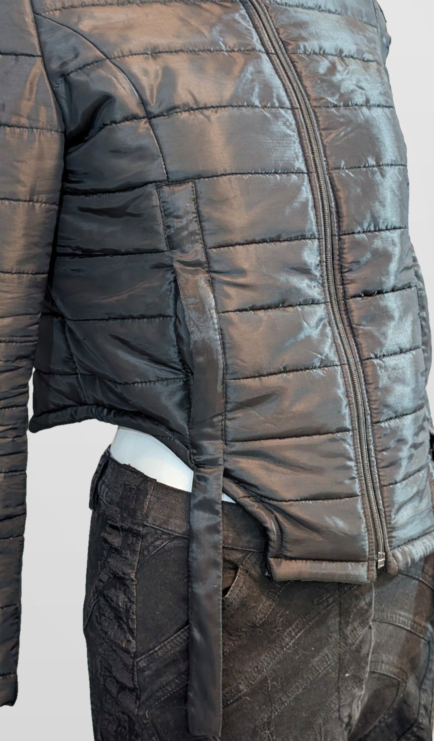 Close detail of the Black Nova Puffer side seam, zip, quilting and hanging side strap, framed just below the strap end