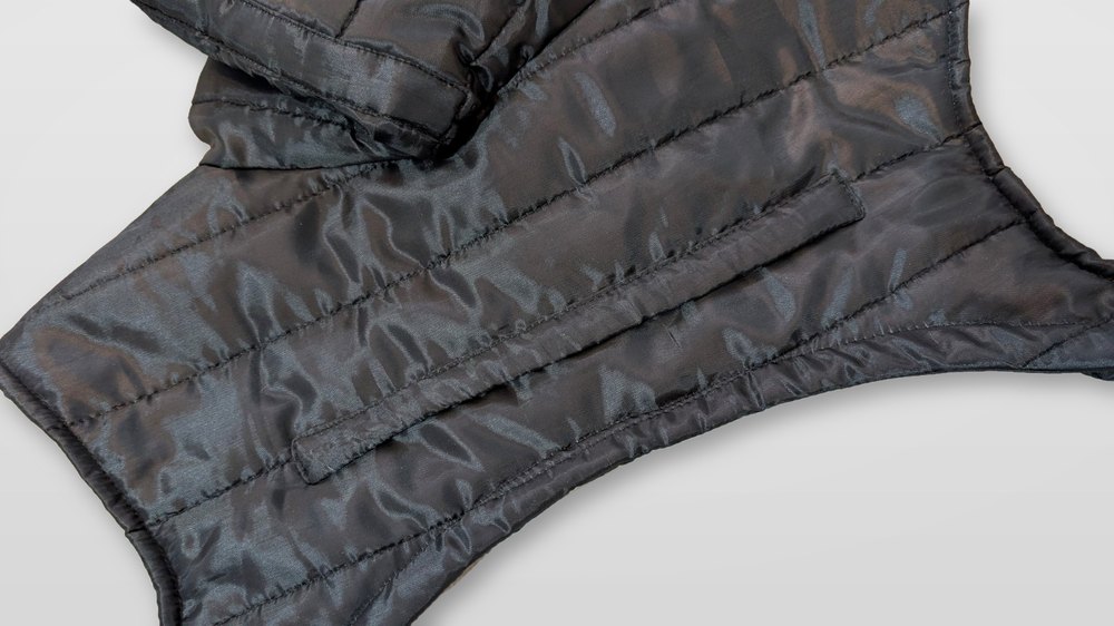 Close-up of quilted black fabric and a sleeve panel on a pearl-grey surface
